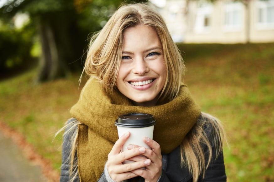 Dame står ute med kaffekopp og skjerf